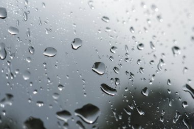Yağmurlu bir günde cam camdaki yağmur damlalarının kasvetli ve soyut arkaplanı. Yoğunlaşmanın dengesiz dokusu ve su damlaları sakin melankoli hissi yaratır.