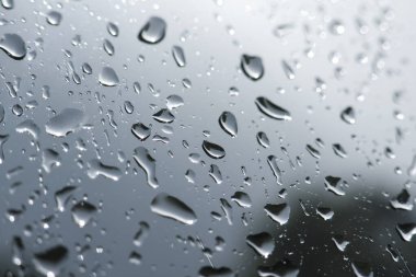 Melankolik yağmur damlası manzarası ve ıslak cam üzerindeki saf su. Gri kasvetli hava, şeffaf yüzey üzerinde yoğunlaşma ile soyut bir arkaplan yaratır