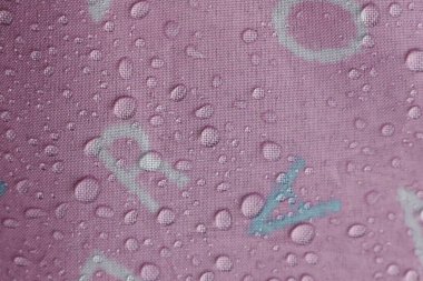 Canlı pembe tekstil yüzeyi birçok parlak su damlacıklarına ev sahipliği yapar, büyüleyici bir doku yaratır ve onun dayanıklı, muhtemelen su geçirmez, kalitesini vurgular. yumuşak ışık her berraklığı yansıtır