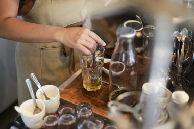 Kafede bir önlükteki baristaya odaklanmış bardakta içki karıştırıyor. Bu hazırlık profesyonellerin çay ya da ahşap tezgahta kokteyl yaptığını gösteriyor.
