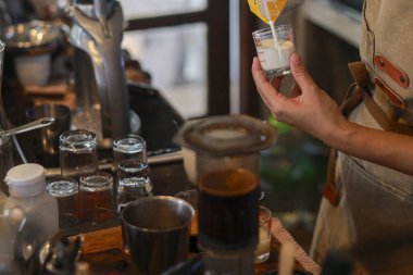 Özel kahve içeceği için bardağa süt dolduran odaklanmış barista. Profesyonel el, kahve makinesi ve ekipman ile sıcak bir kafede sabah içkisi hazırlar.
