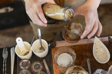 El yapımı kahve içeceği, şişeden bardağa soğuk içecek. Kafedeki bu odaklanmış hazırlık, taze içecek hazırlama sanatsal sürecini gösteriyor.