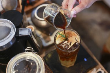 Odaklanmış kahveci ferahlatıcı bir içecek hazırlıyor, soğuk bira için bardağa koyu kahve koyuyor. Kafede canlandırıcı bir buzlu kahve yapma süreci tatmin edici.