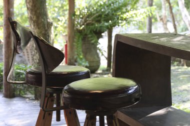 Sessiz, sakin bir açık hava sahnesi, iki kır evi ahşap sandalye ve masa. Yeşil doğa ve yapraklarla çevrili eski mobilyalar huzur verici ve rahatlatıcı bir atmosfer yaratır.