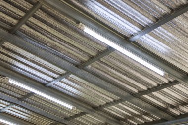 Metal çatı yapısı olan Stark endüstriyel depo tavan arkaplanı. Uzun floresan lambalar çelik kirişe asılarak işlevsel aydınlatma yaratır.