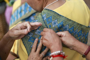 Geleneksel elbiseyi, son sınıf öğrencisinin hazırlanmasına göre ayarlamaya yardım ediyorum. Süslü, desenli kıyafet hazırlığı kültürel tören için nazik bir bakım ve destek anı gösteriyor.