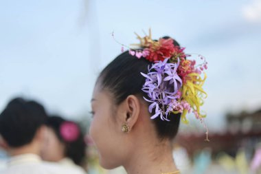 Saçında renkli çiçek desenli çiçekli zarif bir Asyalı kadın. Kültür festivali için geleneksel updo saç stili sakin doğal güzelliği gösteriyor