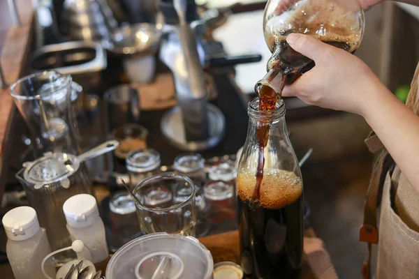 Odaklanmış kahve ustası taze yapılmış el sanatları soğuk kahve şişesini cam şişeye dolduruyor. Yerel kafede tazeleyici içeceğe yönelik dikkatli bir içecek hazırlığı yapılmasına dikkat edilmektedir.