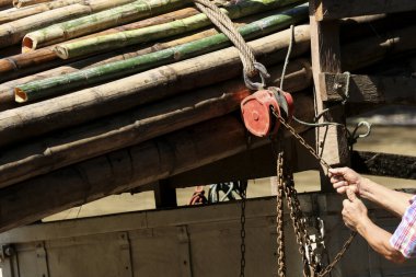 Ağır bambu direklerini kaldırmak için metal zincir çeken işçiler. Bu el emeği kırsal alandaki inşaat alanında güç ve sanayi gösteriyor.