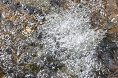 Temiz akarsu yüzeyinde kaynayan su kabarcıklarının tazelenmesi. Bu soyut arka plan kayalar üzerinde enerjik, saf ve canlı doğal su hareketlerini gösteriyor.