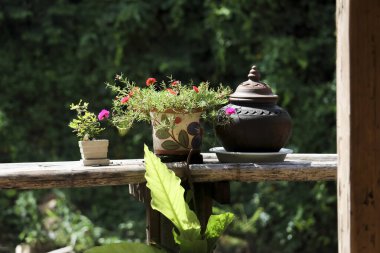 Geleneksel çömlek, kavanoz ve çiçekli süsleme sahnesi. Ekran yemyeşil doğa arka planına karşı kırsal ahşap korkuluklarda oturur