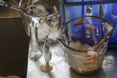 Kirli ölçü kabı ve camla dolu kirli mutfak lavabosu köpük kalıntılarıyla dolu. Yıkanmamış aletler temizlik bekliyor. Yemek pişirdikten ya da pişirdikten sonra tipik ev işleri.