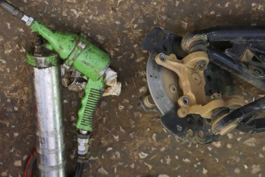 Kirli zeminde yeşil yağ tabancası ve araç fren ayarlayıcısının yakın görüntüsü. Bu endüstriyel çekim, atölyedeki profesyonel onarım ve bakımın özünü yakalar.