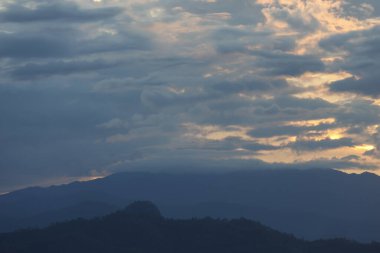 Gün batımında güzel bulutlu gökyüzüne karşı dramatik bir dağ silueti. Huzurlu manzara huzurlu akşam ışığını gösteriyor. Karanlık, kasvetli bulut örtüsünü kırıyor.