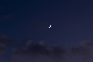Hilal ay, koyu mavi gece gökyüzünde parlıyor. Karanlık bulutların üzerindeki sakin atmosfer. Huzurlu gökyüzünün güzel astronomik manzarası