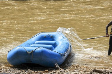 Mavi şişme botu çamurlu nehir suyundan kıyıya çeken adam. Açık hava macera eğlencesi su sporu gezisi için hazırlık ve çaba gösteriyor.
