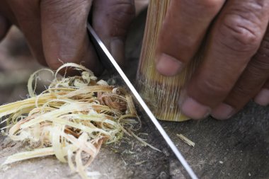 Bıçakla bambu oymaya odaklanmış geleneksel hünerlerini sergileyen işçi elin yakın çekimi. El yapımı iş için ahşabı ince lifli tıraş etmeyi içeren detaylı bir zanaat.