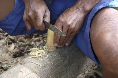 Eli yıpranmış odaklanmış bir adam keskin bıçakla geleneksel aletleri oyuyor. Bu el işi, balık ağı için gerekli ekipmanları hazırlamada beceri ve uzmanlık gösteriyor.
