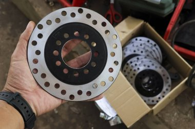 Tamirat ve tamirat için yeni motor diski fren pervanesi parçasını garajda tutarken yakın çekim. Eski otomotiv bileşenini değiştirmeye hazırlanılıyor