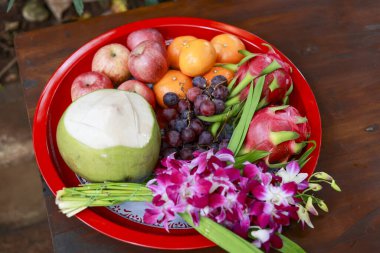 Asya 'da kültürel tören için kırmızı tepside canlı meyve sunumu. Geleneksel orkide, taze çiçek ve ejderha meyvesi düzenlemeleri bolluk ve saygıyı temsil eder.
