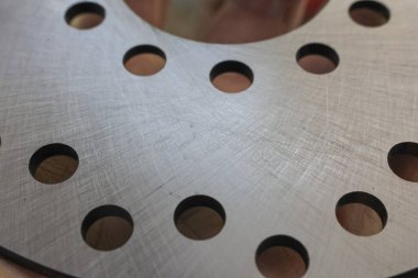 Metal otomotiv fren diski yüzeyini kapatın. Çelik parçası, soğutma, güçlü ve hassas endüstriyel bileşenler için delinmiş deliklerle detaylı dokuyu gösteriyor.