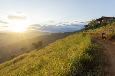Gün batımında çimenli tepe boyunca bisiklet süren huzurlu bir insan. Altın güneş, huzurlu kırsal alan ve manzara üzerine sıcak bir parıltı saçar.