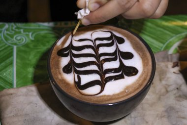 Yetenekli barista el sıcak mocha içeceği üzerinde güzel kahve sanatı yaratıyor. Çikolata sosundaki sanatsal desen ve bu içecekteki köpük sıcacık ve sıcak bir içecek sağlar.