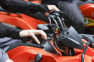 Odaklanmış eller turuncu bir ATV dörtlü araç kullanmaya hazır gidona. Heyecan verici açık hava macerası, bu off-road aktivitesi hız, güç ve aşırı spor heyecanını temsil ediyor.