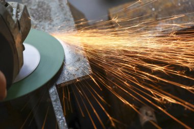 Atölyedeki endüstriyel bir aletle metal öğüten işçilere yaklaş. Parlak sıcak kıvılcımlar çelikten uçar, yoğun bir ışık ve ısı gösterisi yaratır.