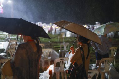 Dışarıda yağmurlu bir gecede hasta bir kalabalık toplandı. Bir kadın şemsiye tutuyor, sağanak yağış sırasında şovu seyrediyor, kötü hava koşullarında sabırla bekliyor.