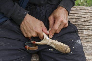 Elde ahşap sapan tutan adam, köy silahı yaparken konsantrasyonunu gösteriyor. Basit ve odaklanmış yaşam tarzını gösteren bir açık hava aktivitesi
