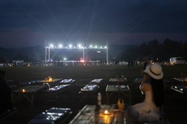 Seyirciler arasındaki kadın gece konser veya festival izlemekten hoşlanıyor. Açık hava olayının aydınlık bir sahnesi var. Kalabalığı rahatlatmak için büyülü bir ortam yaratıyor.