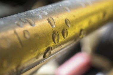 Pirinç metal yüzeyini temiz su damlası formasyonuyla kaplayan detaylı makro. Altın doku yoğunlaşmanın sakin ve odaklanmış arkaplan görüntüsü oluşturduğunu gösterir