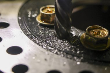 Güçlü matkap ucu, metal levhada delik açıyor. Atölyedeki odaklanmış delme işlemi, metal cücelerin havada uçuştuğu hassas bir üretim olduğunu gösteriyor.