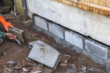İnşaat işçisinin beton blok temeli üzerine odaklanmış ağır işçiliği. Eldivenli adam ev onarımı projesi için havan topu ve duvar malzemesi kullanıyor.