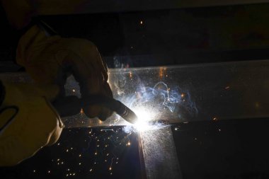 Üretim sırasında çelik metali kaynaklayan odaklı endüstriyel işçiler. İnşaat alanında güvenlik eldiveni ile korunan parlak kıvılcımlar üretimden uçar.