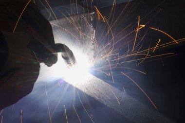 Yetenekli işçilerin yoğun endüstriyel kaynak çalışmaları. Kaynakçı çelik üzerinde metal üretiyor, inşaat sırasında parlak ışık ve birçok kıvılcım yaratıyor.