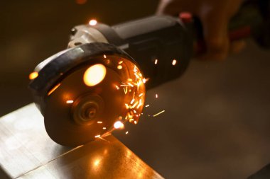 Metali kesmek için bir açı öğütücü kullanarak yoğun bir şekilde yaklaşan işçiler parlak kıvılcımlar yaratıyor. Atölyedeki sanayi çalışmaları güç ve hassasiyeti gösteriyor