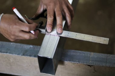 Metal tüpü cetvelle ölçen işçi elini kapat. Atölyedeki işaretleme sürecine odaklanan bu inşaat işi, beceri ve endüstriyel hassasiyet gösteriyor