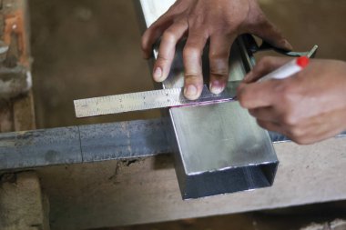 Metal kirişi kare cetvelle işaretleyen odaklanmış işçi el ölçümlerini kapat. Çalışkan zanaatkar fabrikadaki inşaat ve metal işlerinde hassasiyet gösteriyor.