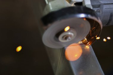 Metal kesen güçlü bir açı öğütücü kullanarak yoğun endüstriyel çalışma. Atölyede dönen diskten parlak turuncu kıvılcımlar uçuşuyor. Üretim sürecini kapatıyorlar.