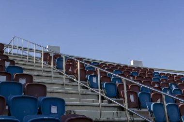 Açık gökyüzünün altındaki açık hava stadyumunda boş mavi koltuk. Sakin ve ıssız sahneler, mükemmel spor arka planı için tribün, koridor ve metal parmaklıkları gösteriyor.