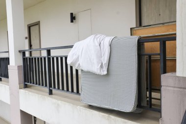 Modern apartman balkonunun siyah korkuluklarında beyaz tişörtlü ve gri yastıklı sıradan bir sahne. Ev işlerinin basit, sessiz bir temsili