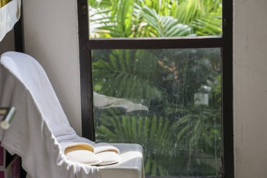 Açık bir kitap ve terliğin sakin ve rahatlatıcı bir sahnesi güneşli pencerenin kenarında dinleniyor yemyeşil yaprakların güzel manzarası evde huzurlu ve sessiz bir ortam yaratıyor.