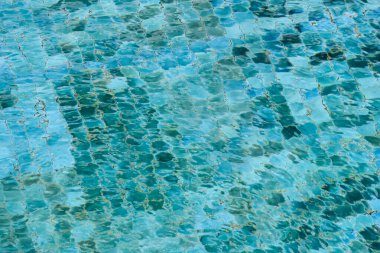 Yüzme havuzundaki berrak mavi suyun soyut arkaplanı. Yüzeyde dalgalanma dokusu var, çarpık fayans deseni oluşturuyor ve sakin, sakin bir yaz gününü çağrıştırıyor.