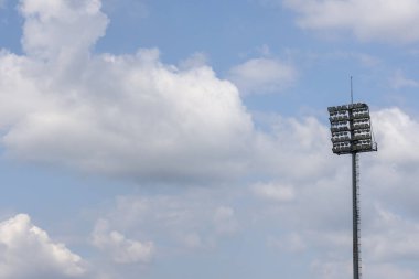 Uzun stadyum ışık direği beyaz bulutlu huzurlu mavi gökyüzüne karşı duruyor. Akşam maçına hazır bir açık hava spor lambası. Sessiz gündüz aydınlatma arkaplanı