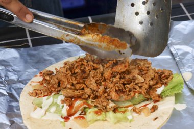 Şef lezzetli bir shawarma kebap dürümü hazırlıyor. Taze baharatlı et, marul ve ekmek üzerine sos. Savory sokak yemekleri açık hava pazarında sergileniyor.