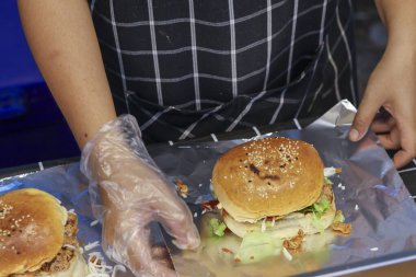 Şef folyoyla lezzetli bir hamburger hazırlıyor. Önlük ve eldiven giymiş profesyonel bir aşçı fast food restoranı siparişi için mutfağa taze yemek koyar.