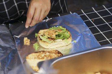 Şef alüminyum folyoda yeşil marullu lezzetli taze burger hazırlıyor. Bu iştah açıcı fast food sandviçi sokak yemekleri için paketleniyor.
