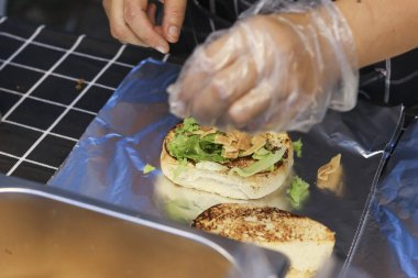 Şef eldiven giymiş, mutfakta yemek hazırlamakla meşgul. Hijyen ve kaliteli malzemelere odaklanmış müşteriler için taze hamburger yemeği pişirmek.